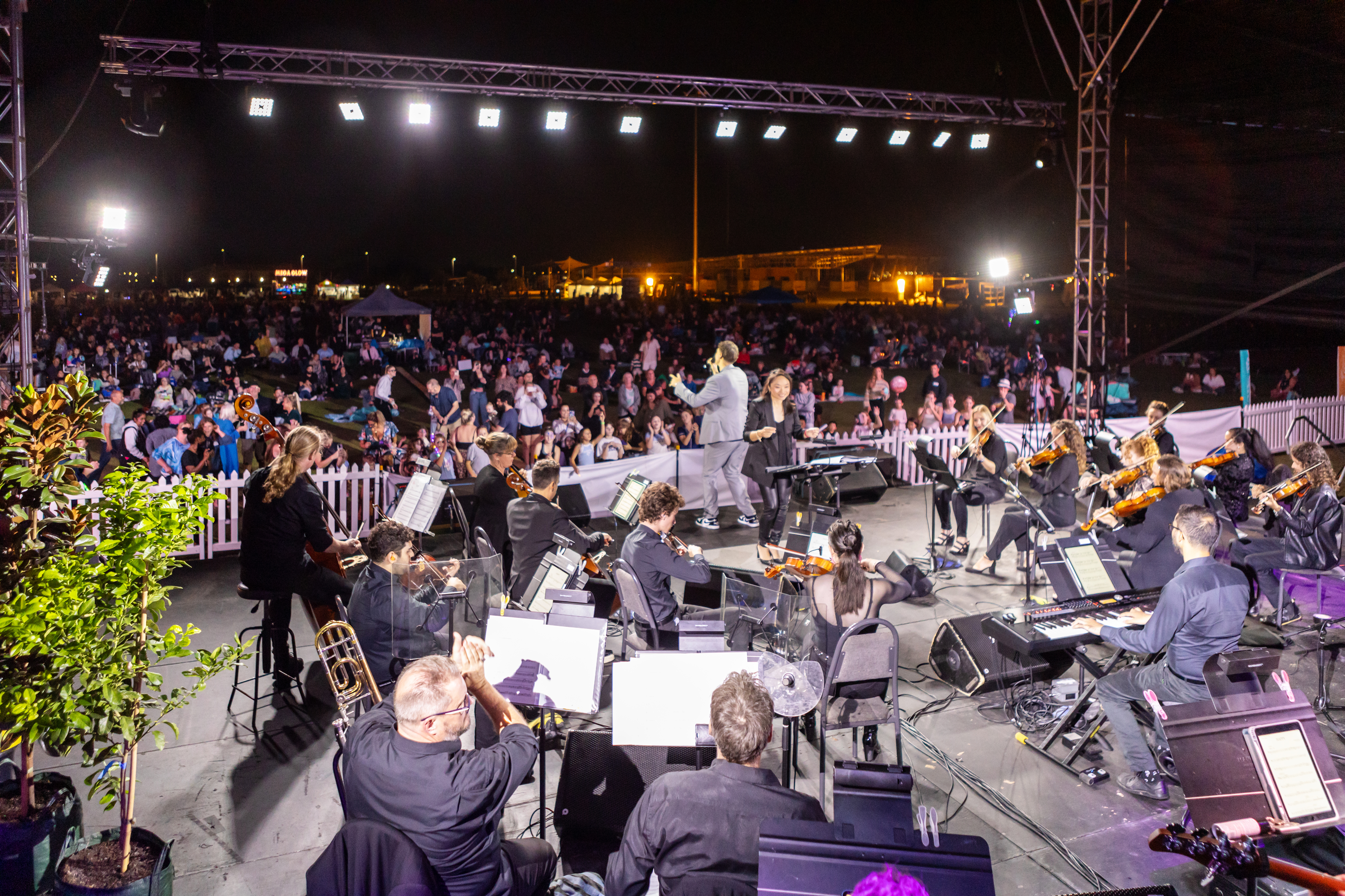 Live symphony orchestra performing on stage with a singer in front of a large outdoor crowd at night.