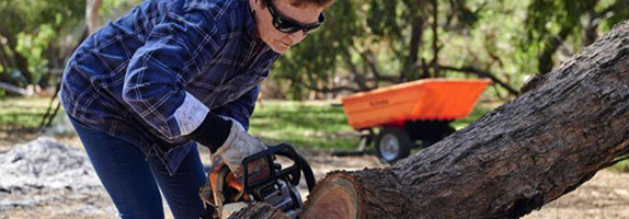 Woman using chainsaw to clear fallen tree